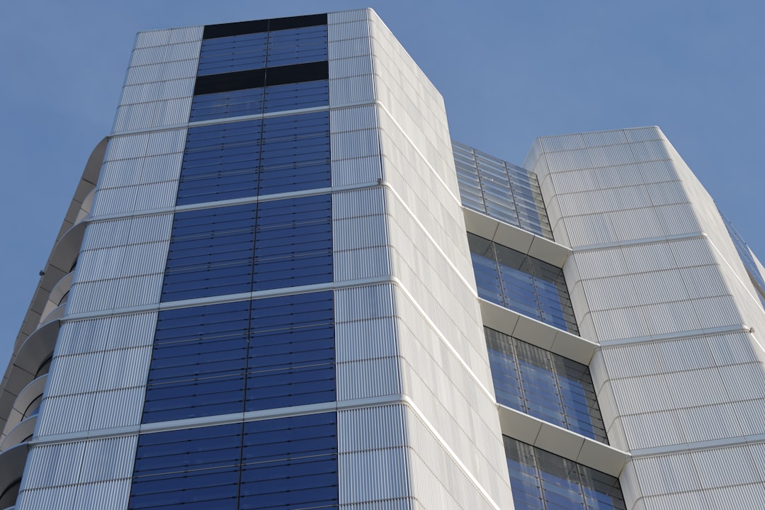 A close-up view of a modern office building with blue-tinted windows and metallic panels. The building has a sleek design with alternating sections of glass and metal.